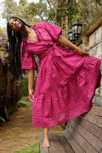 model with braids wearing a pink lace wrap dress poses in a garden