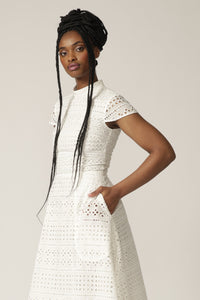 Side view of a model with braids wearing a white capped-sleeve lace dress with pockets