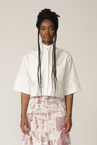 Model with braids wears a white cropped jacket with high neck and printed skirt
