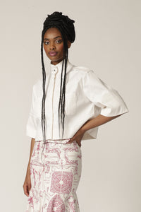 Model with braids poses in a white cropped jacket with high neck and printed skirt