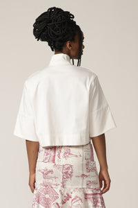Back view of a Model wearing a white cropped jacket with high neck and printed skirt