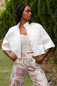 model with braids wearing a printed toile pant and white cropped jacket poses in a garden