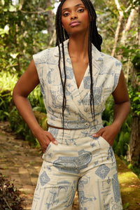 model with braids wearing a matching blue toile sleeveless jacket and pants poses in a garden
