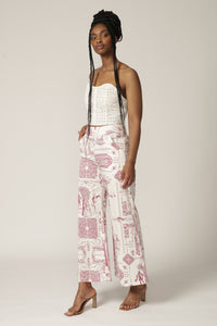 Model with braids wears a white lace corset and red and white patterned pants