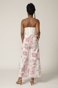 Back view of a model with braids wearing a white lace corset and red and white patterned pants
