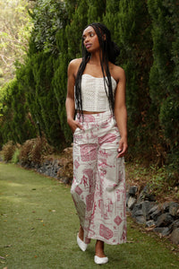 model with braids wearing a lace corset and red toile pants poses in a garden