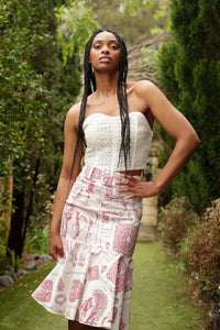 model with braids wearing a red toile ruffle skirt and lace corset poses in a garden