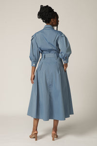 Back view of a model with braids wearing a blue shirt dress with puffed sleeves and matching belt